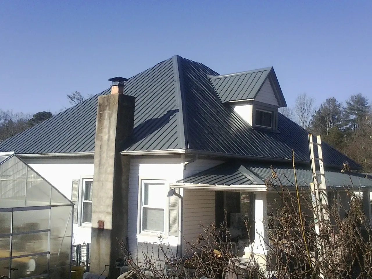 Dark blue standing seam metal roof on a white farmhouse with dormer — Slate & Tile Roof Repair by Roofing Brothers in Lometa