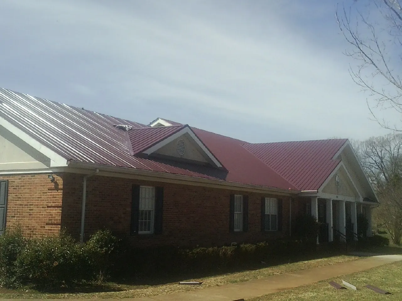 Red metal roof with gabled entries on a long brick building, from a Hail Damage Roof Repair job in Lometa