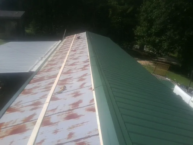 Old rusted panels beside newly installed green metal roofing — Wind Damage Roof Repair by Roofing Brothers in Lometa