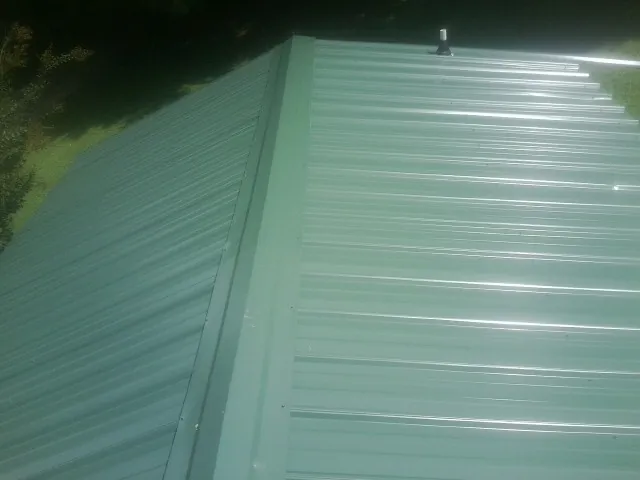 New green metal panels meeting at the ridge of a roof — Flat Roof Repair work by our crew in Lometa