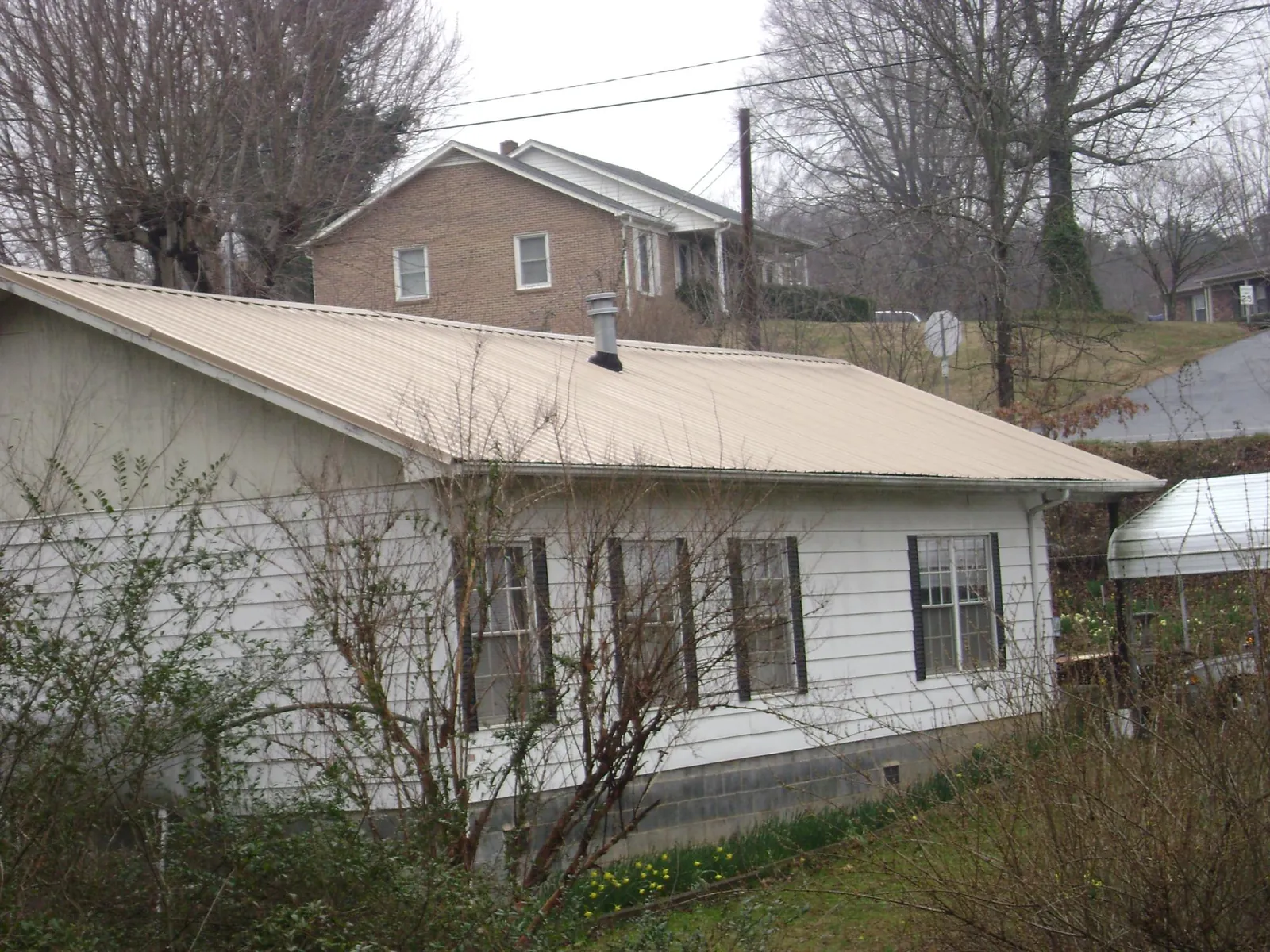 Tan metal roof on a white sided house set into a hillside — Commercial Roofing by Roofing Brothers in Lometa