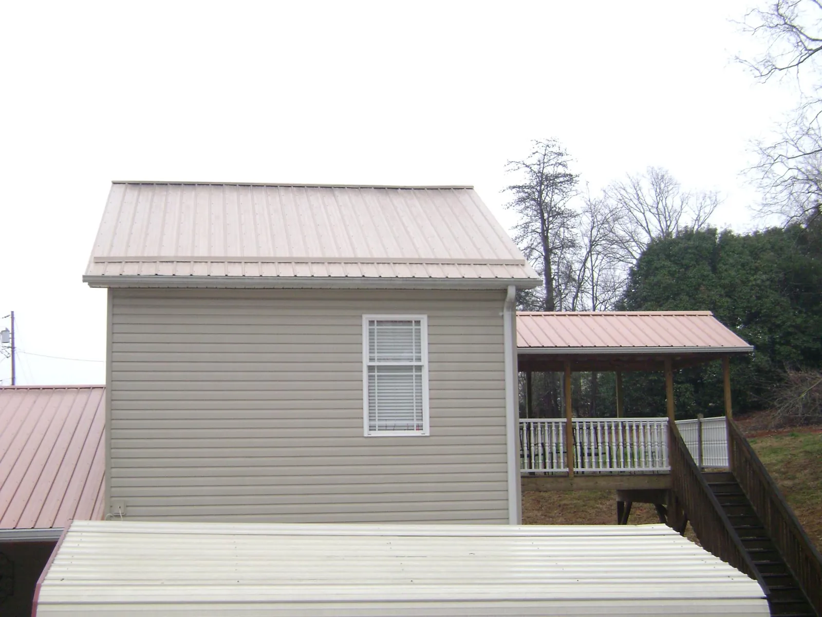 Tan metal roofs on a two story addition and attached porch, from a Roof Replacement job in Lometa
